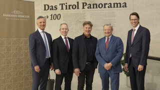 Fünf Männer in Anzügen lächeln in die Kamera. Sie stehen vor einer Wand mit der Aufschrift "Bankhaus Spängler" und "Das Tirol Panorama".