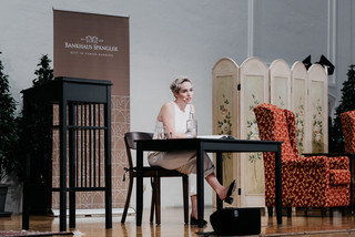 Schauspielerin Verena Altenberger sitzt auf einer schön dekorierten Bühne und hält eine Lesung