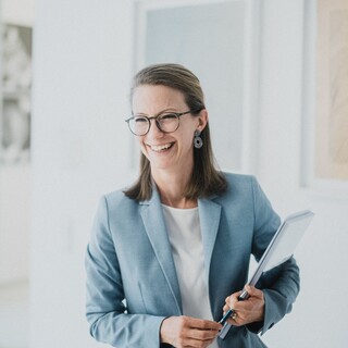 Eine Frau mit kurzen Haaren und Brille lacht freundlich.