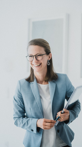 Eine Frau mit kurzen Haaren und Brille lacht freundlich.