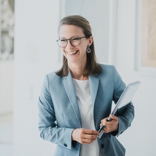 Eine Frau mit kurzen Haaren und Brille lacht freundlich.