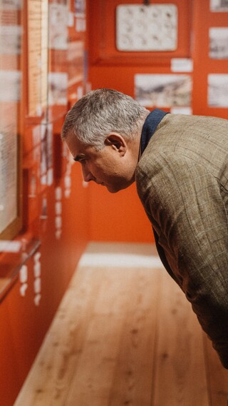 Ein Herr in Anzug liest einen Text auf einer Wand mit historischen Fotografien.