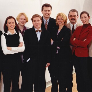 Das Linz-Team im Jahre 2002 Eine lächelnde Personengruppe in eleganter Kleidung posiert vor einer Wand.