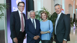 Vier Personen in eleganter Kleidung posieren lächelnd in einem Saal.