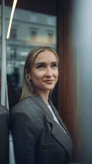 Person in Business-Kleidung steht vor einer Glasfläche und blickt leicht nach oben.