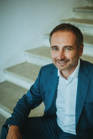 Ein lächelnder Herr in Anzug sitzt auf einer historischen Treppe.