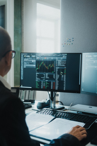 Ein Herr in Geschäftskleidung sitzt vor einem Computerbildschirm mit finanzmathematischen Darstellungen.